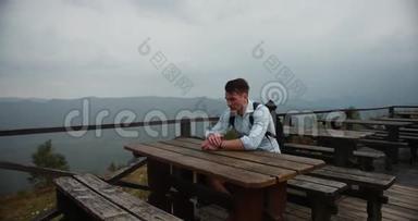 孤独的人在山里。 年轻的帅哥把头靠在手臂上，坐在桌子旁，视野很好
